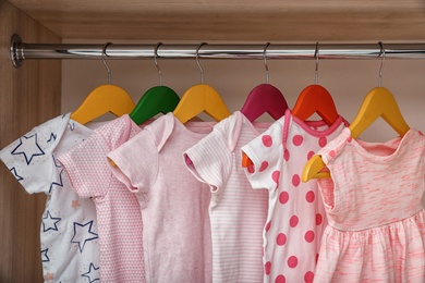 Hangers with baby clothes on rack in wardrobe, closeup