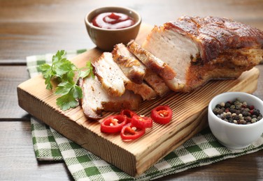 Photo of Pieces of baked pork belly served with sauce, chili pepper and parsley on wooden table, closeup