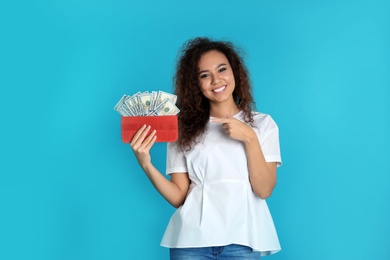 African-American woman with money in wallet on color background