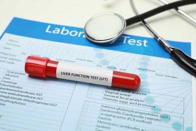 Photo of Liver Function Test. Tube with blood sample, form and stethoscope on table, closeup