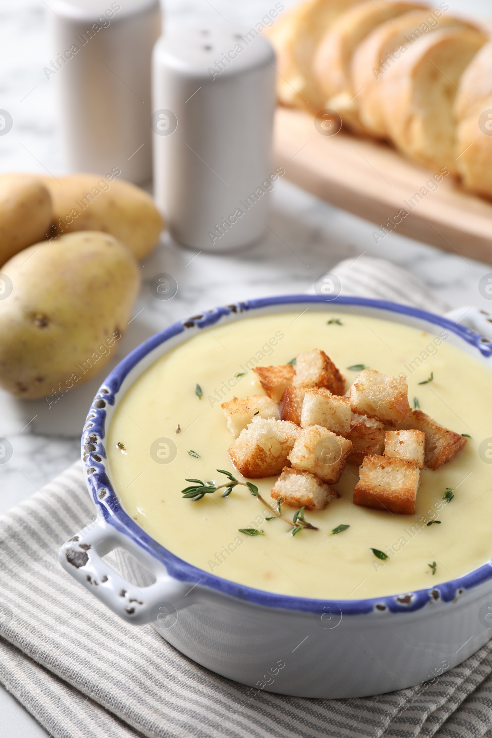 Photo of Tasty potato soup with croutons and rosemary in ceramic pot on white table, closeup