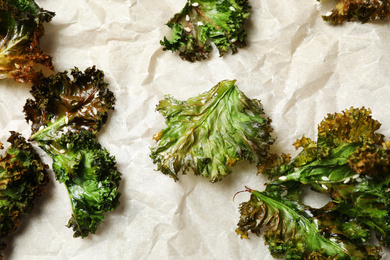 Photo of Tasty baked kale chips on parchment paper, flat lay