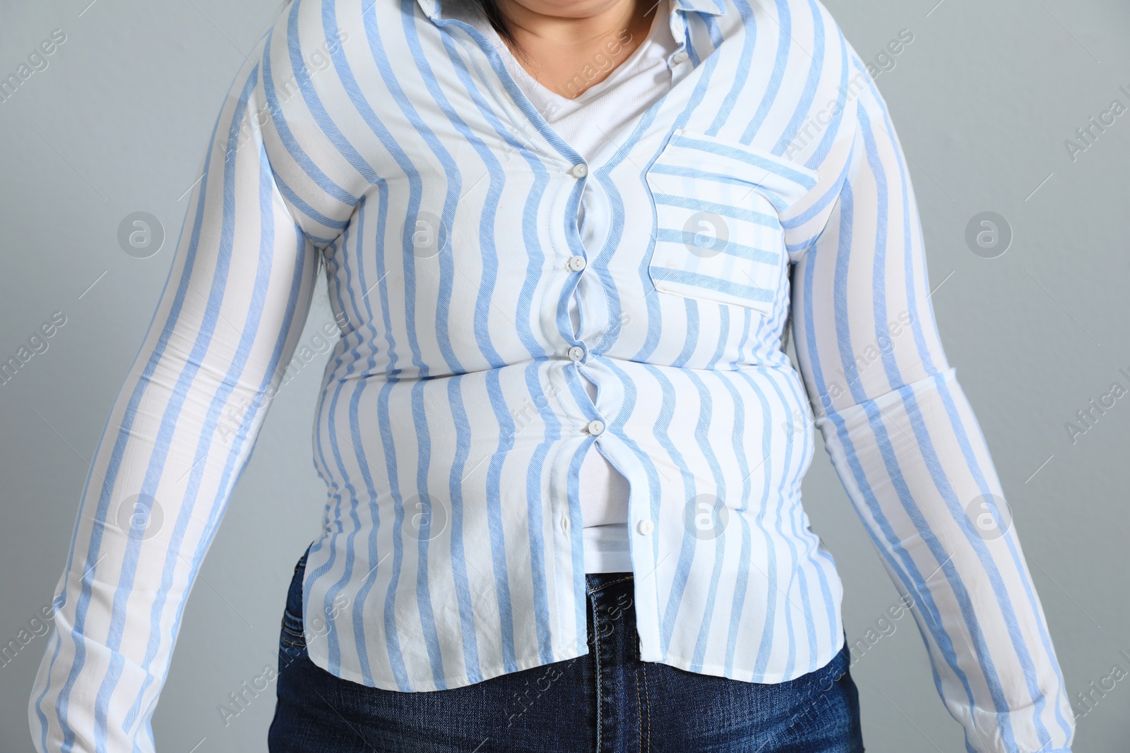 Photo of Overweight woman in tight shirt on light grey background, closeup