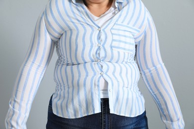 Photo of Overweight woman in tight shirt on light grey background, closeup