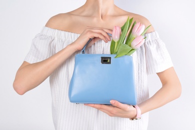 Photo of Stylish woman with handbag and spring flowers against light background, closeup