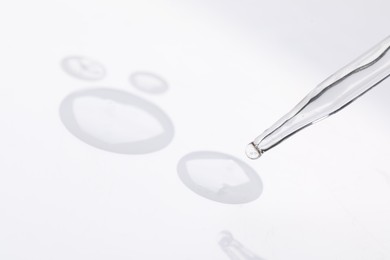 Photo of Glass pipette and transparent liquid on white background, closeup