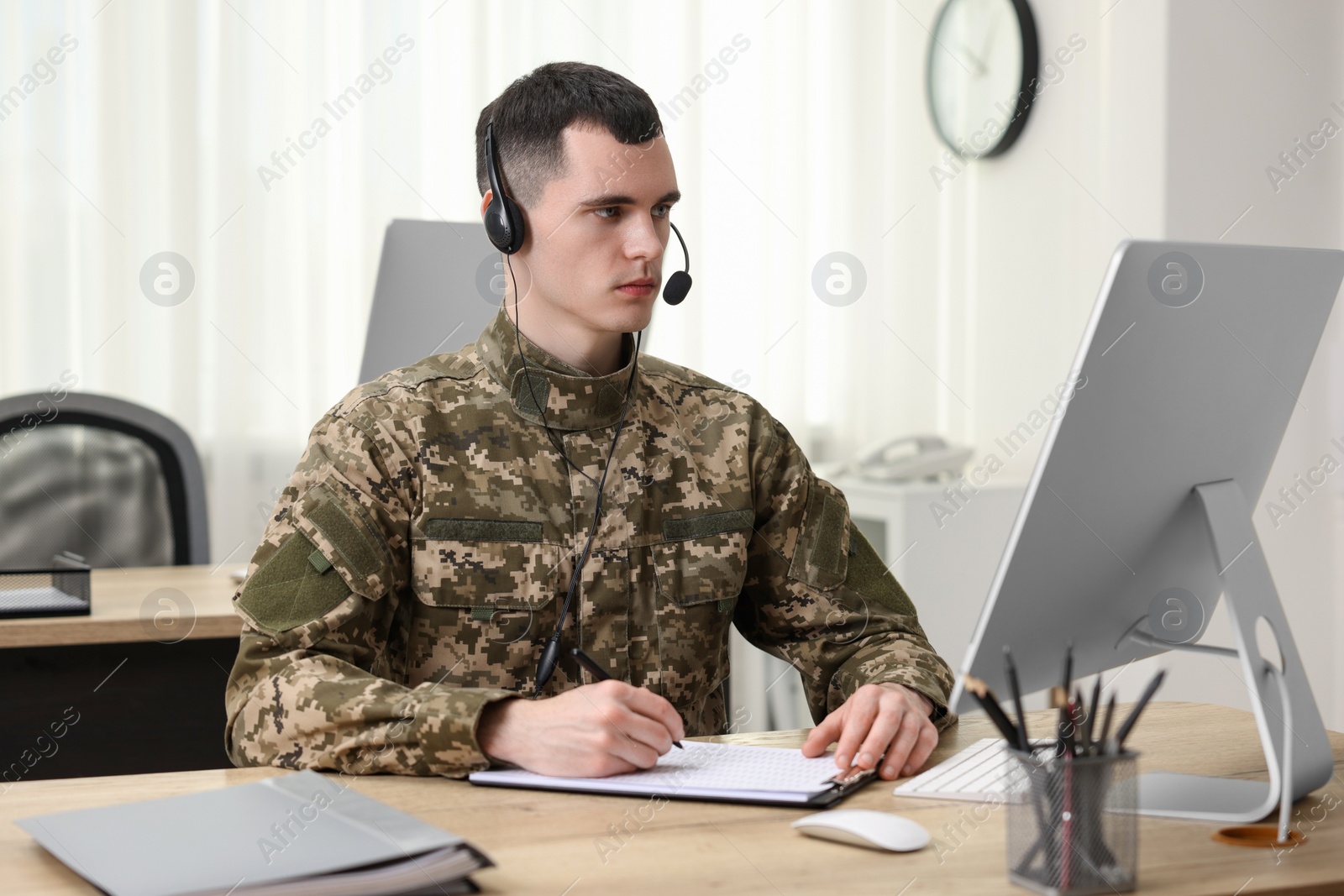 Photo of Military service. Young soldier in headphones working at wooden table in office