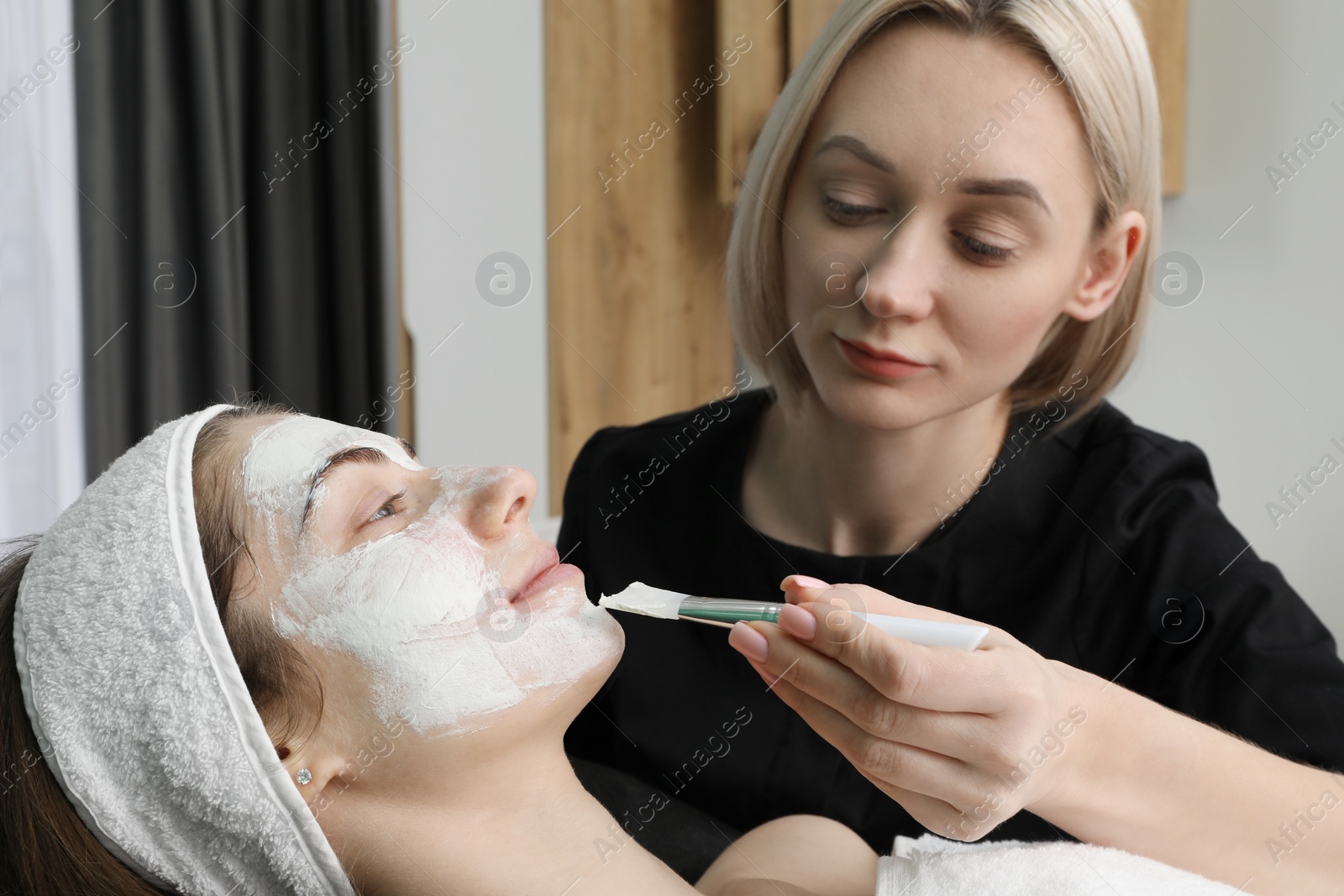 Photo of Cosmetologist applying mask on woman's face in clinic