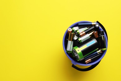 Used batteries in bucket on yellow background, top view. Space for text