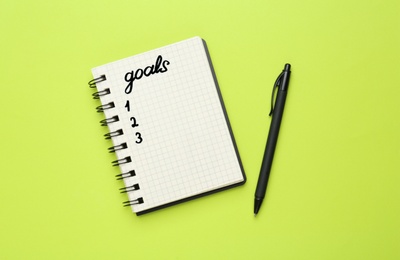 Photo of Notebook with goal list and pen on green background, flat lay