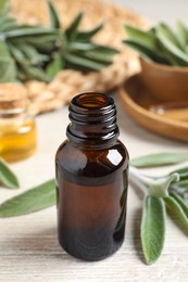 Bottle of essential sage oil and leaves on wooden table