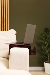 Photo of Laptop on sofa armrest wooden table in room. Interior element