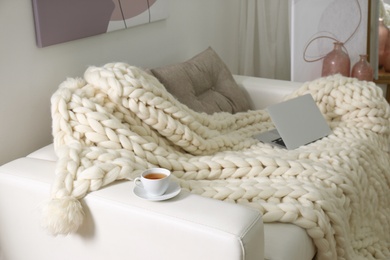 Soft knitted blanket and modern laptop on couch in living room. Interior element