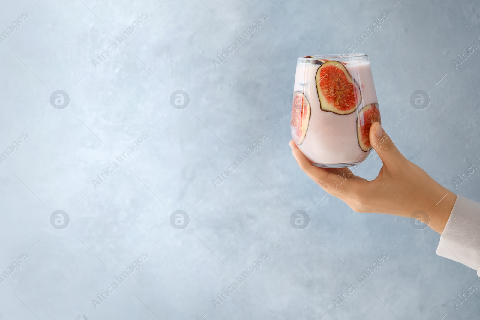 Photo of Woman holding fig smoothie on light blue background, closeup. Space for text