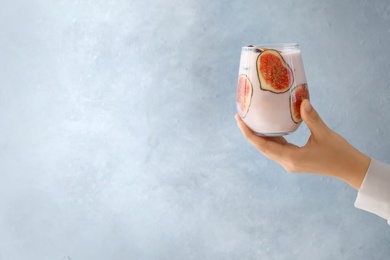 Woman holding fig smoothie on light blue background, closeup. Space for text