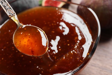 Glass bowl with tasty fig jam and spoon on table, closeup