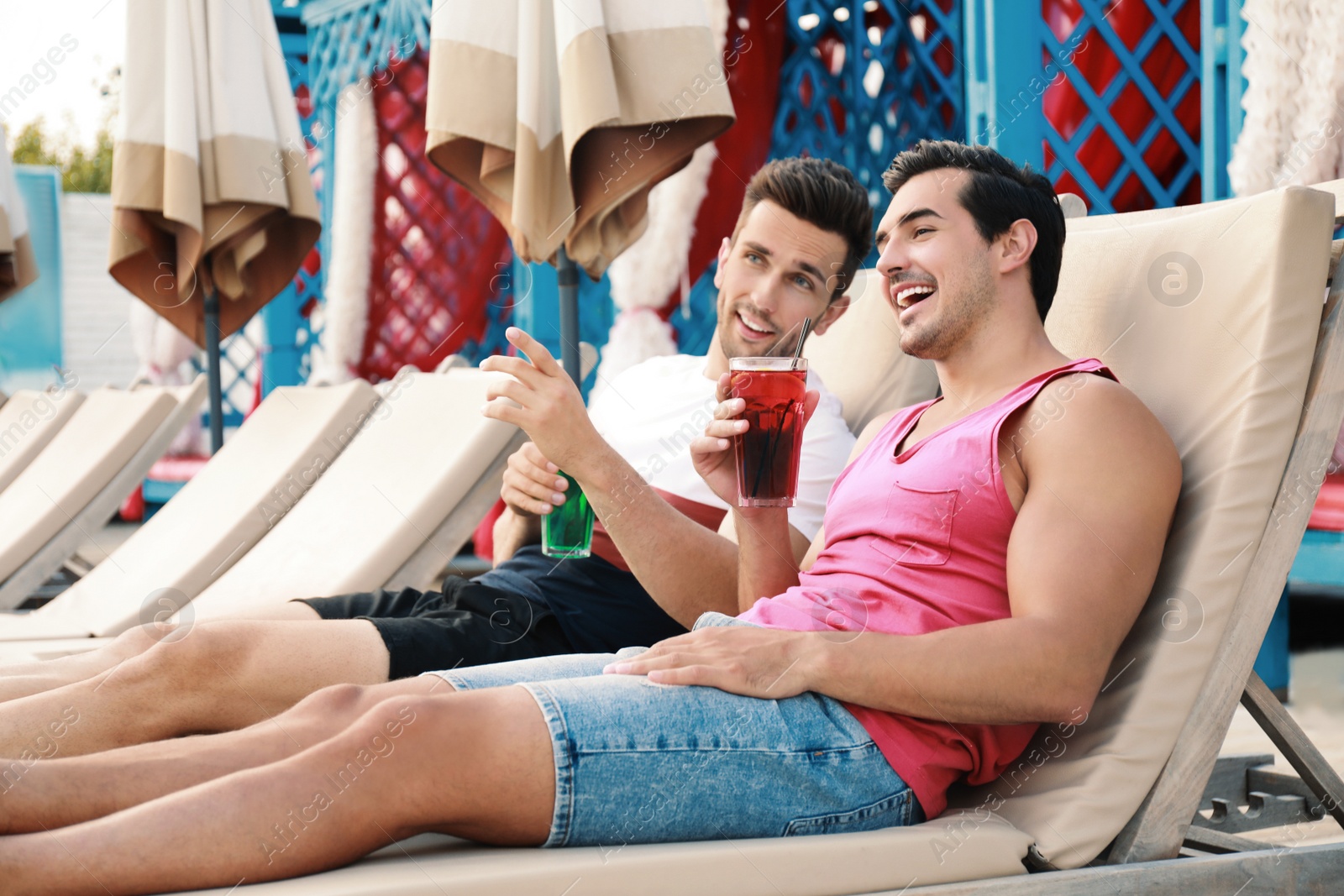 Photo of Happy young friends with fresh summer cocktails relaxing on sunbeds