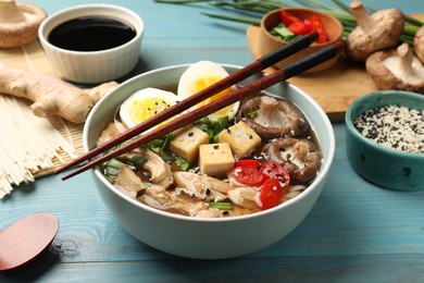 Photo of Bowl of delicious ramen and ingredients on light blue wooden table. Noodle soup