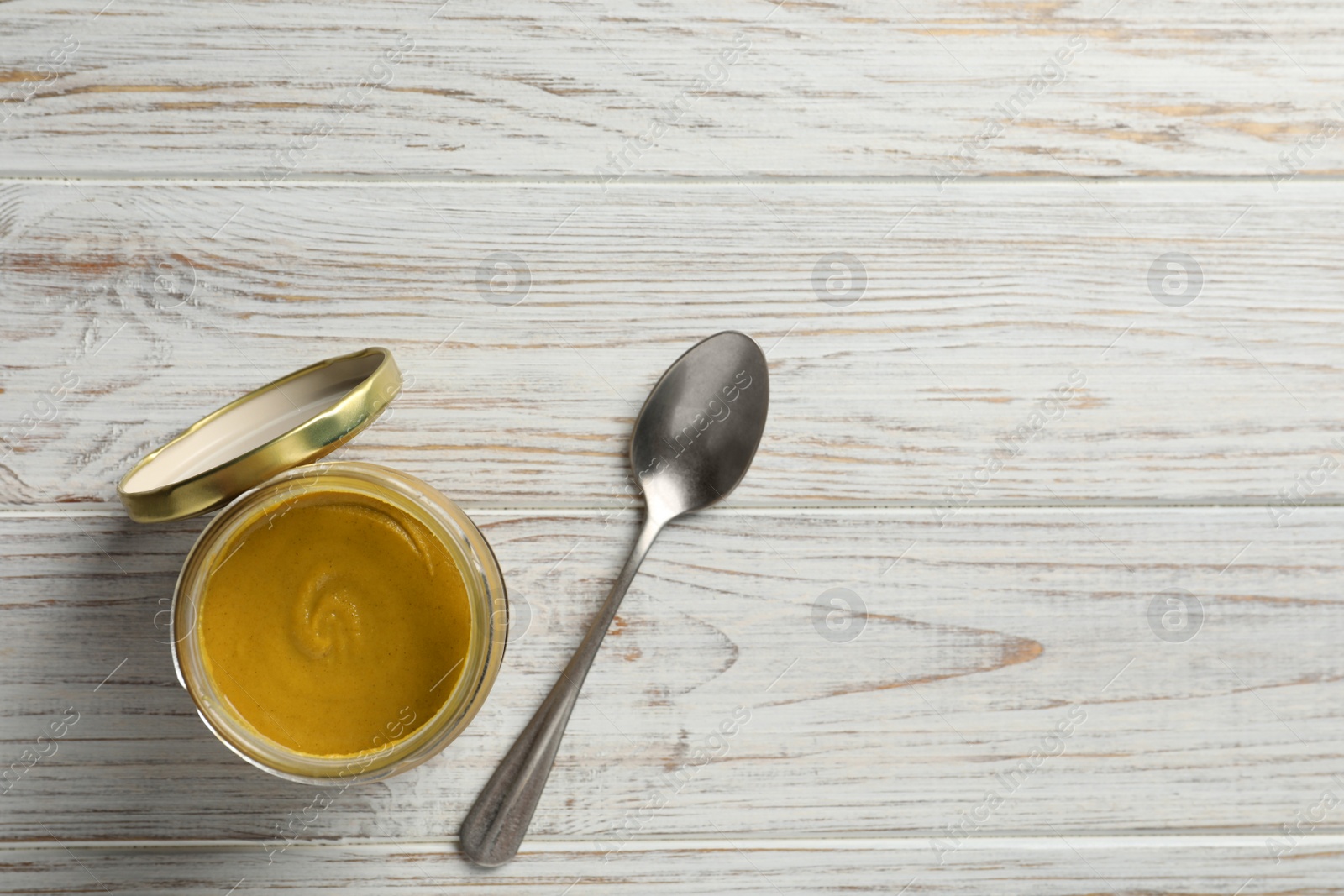 Photo of Spicy mustard in glass jar and spoon on white wooden table, flat lay. Space for text