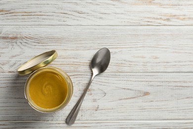 Spicy mustard in glass jar and spoon on white wooden table, flat lay. Space for text