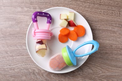 Different nibblers with fresh apple and boiled carrot on wooden table, top view. Baby feeder