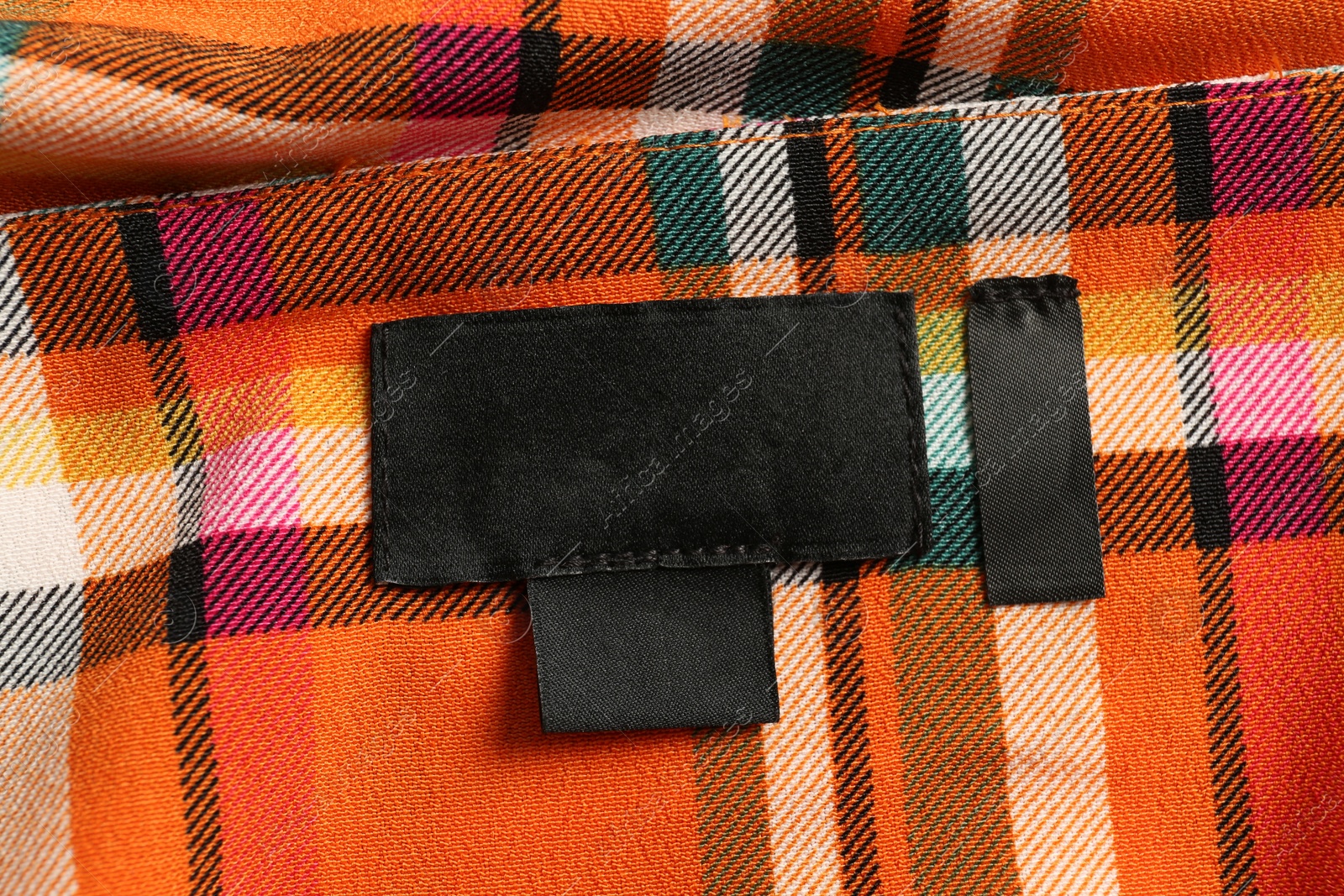 Photo of Blank clothing label on checkered apparel, top view