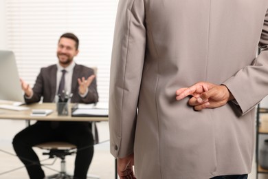 Photo of Employee crossing fingers behind his back while meeting with boss in office, selective focus