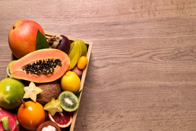 Different tropical fruits in box on wooden table, top view. Space for text