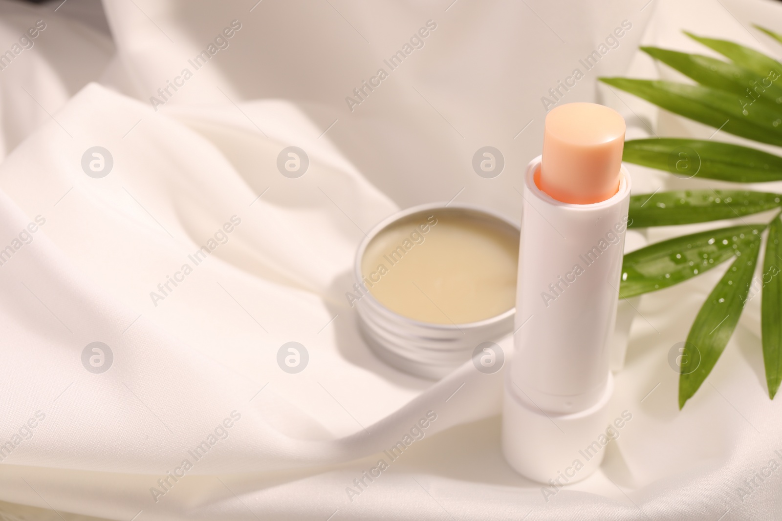 Photo of Lip balms and palm leaf on white fabric, space for text