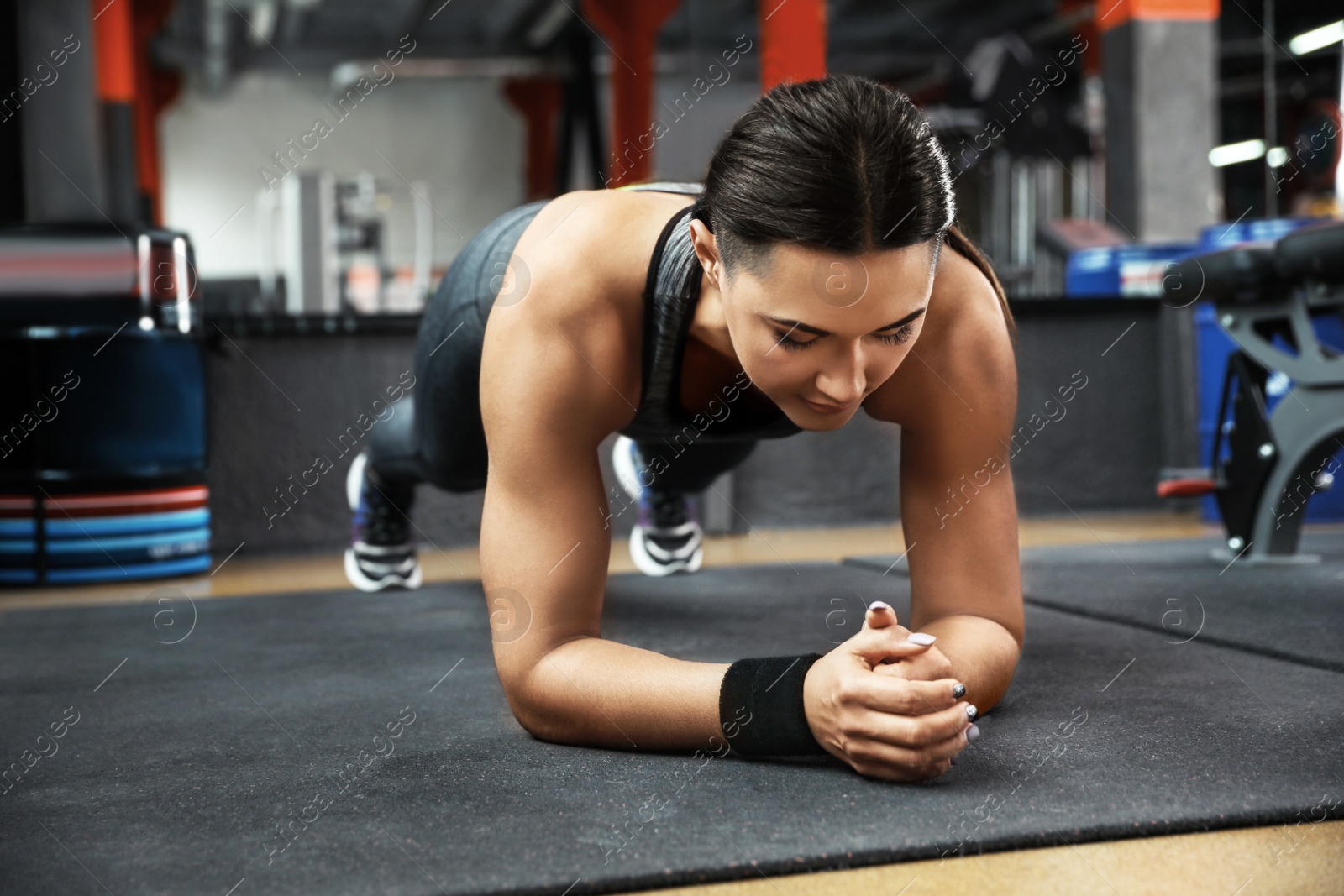 Photo of Young woman doing plank exercise in modern gym