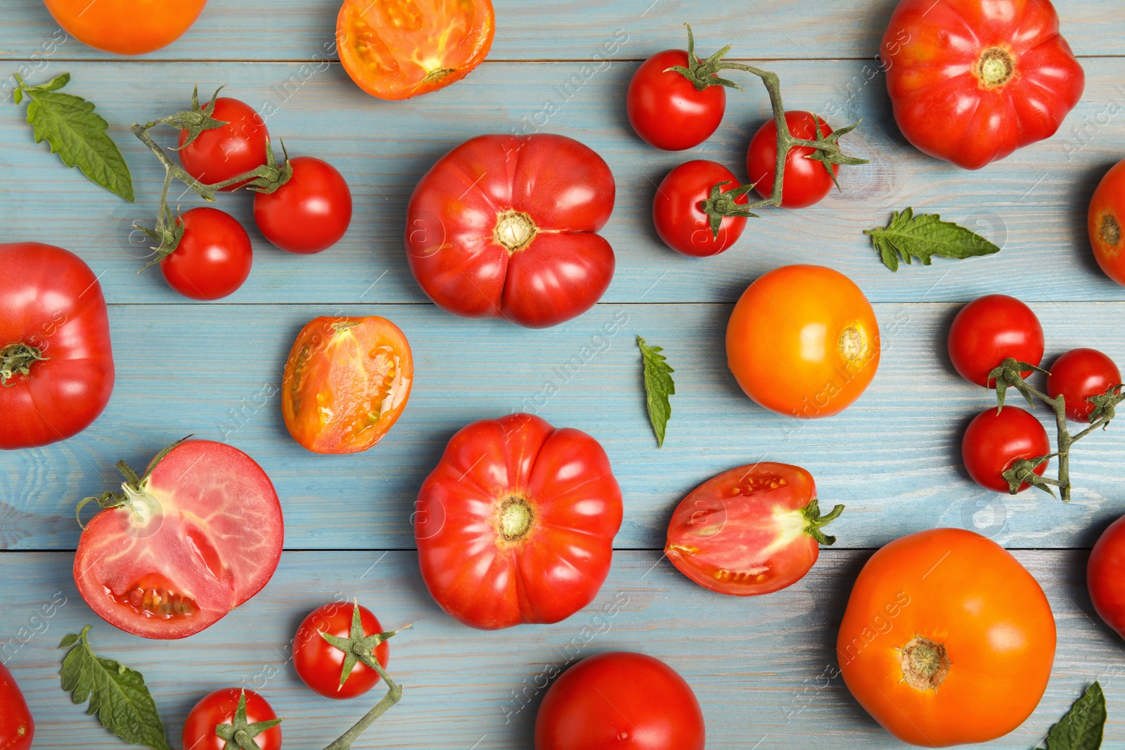 Photo of Flat lay composition with different ripe tomatoes and leaves on light blue wooden table