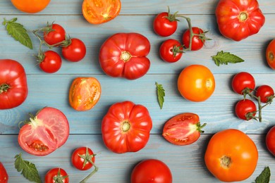 Photo of Flat lay composition with different ripe tomatoes and leaves on light blue wooden table