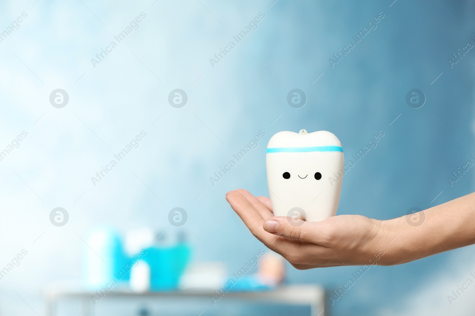 Photo of Dentist holding model of tooth with cute face on blurred background. Space for text