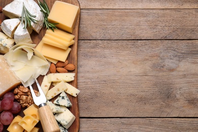 Photo of Cheese plate with grapes and nuts on wooden table, top view. Space for text