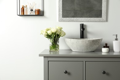 Vase with beautiful white roses and toiletries near sink in bathroom, space for text