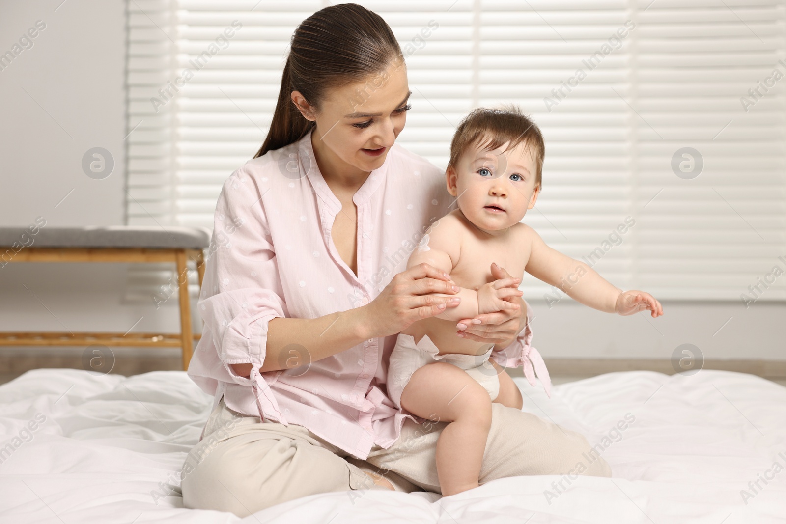 Photo of Happy mother applying body cream onto baby`s skin at home