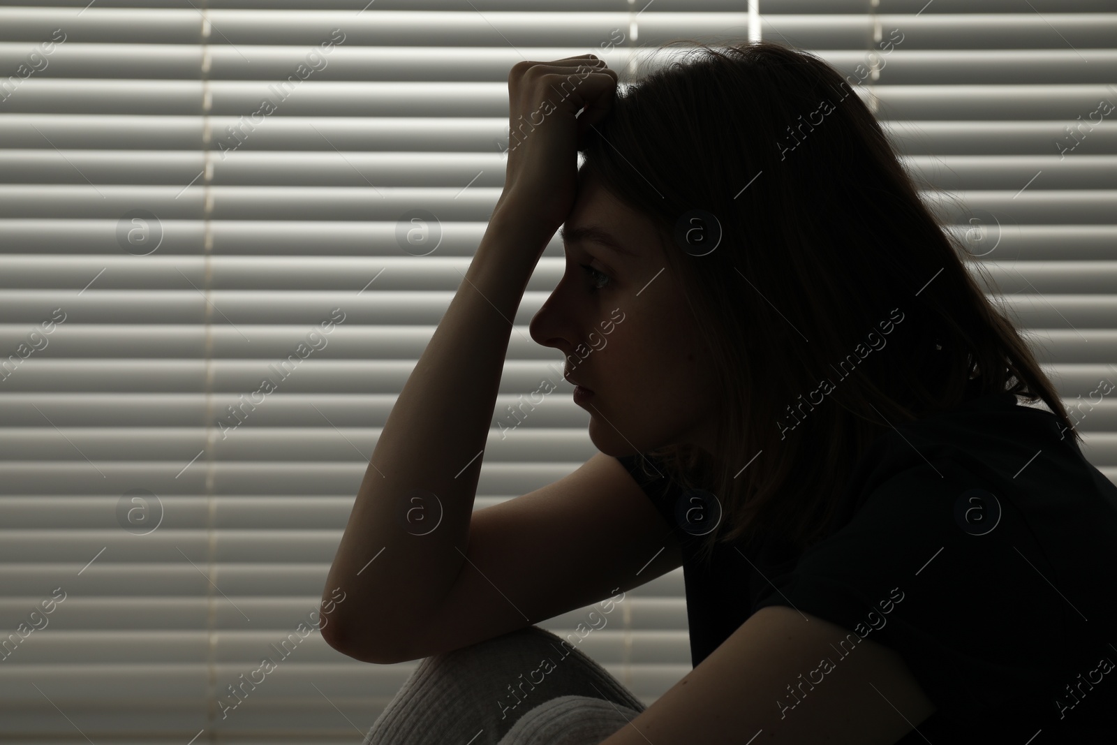 Photo of Sad young woman near window indoors, space for text