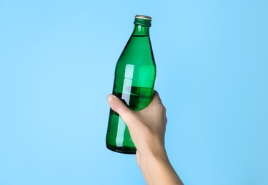 Photo of Woman holding glass bottle with water on light blue background, closeup