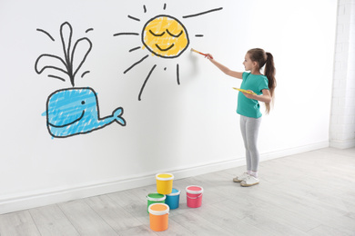Image of Cute child drawing sun and whale on white wall indoors