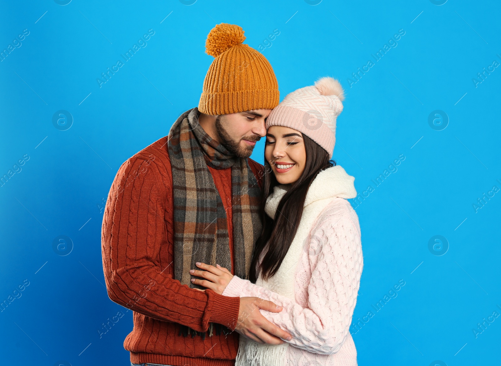 Photo of Happy young couple in warm clothes on blue background. Winter vacation