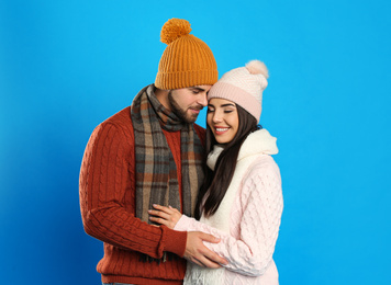 Happy young couple in warm clothes on blue background. Winter vacation