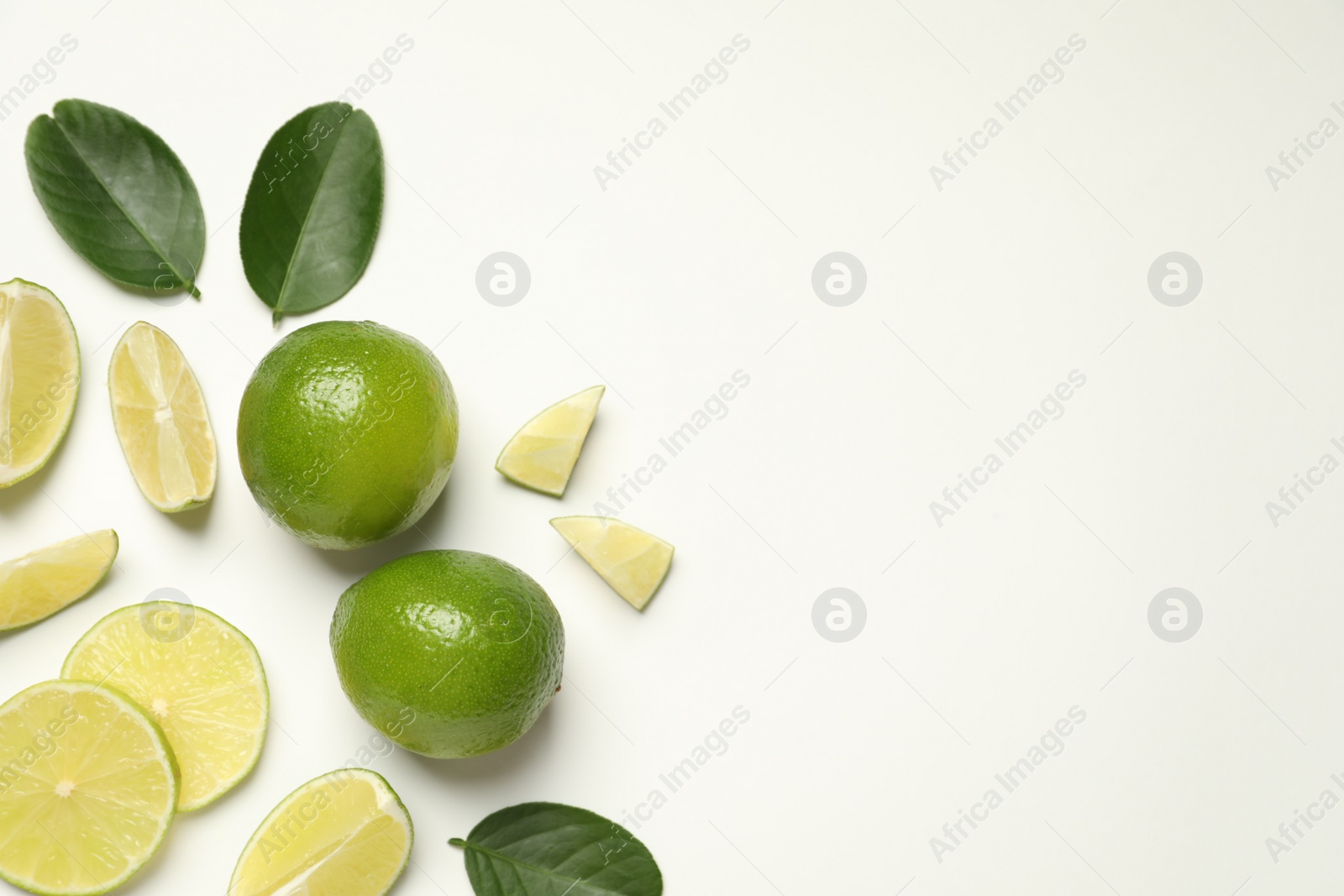 Photo of Whole and cut fresh ripe limes with green leaves on white background, flat lay