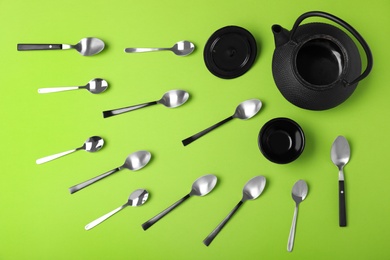 Flat lay composition of spoons, cup and teapot on green background