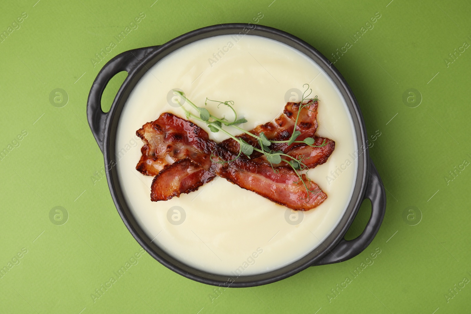 Photo of Delicious potato soup with bacon and microgreens in bowl on green table, top view