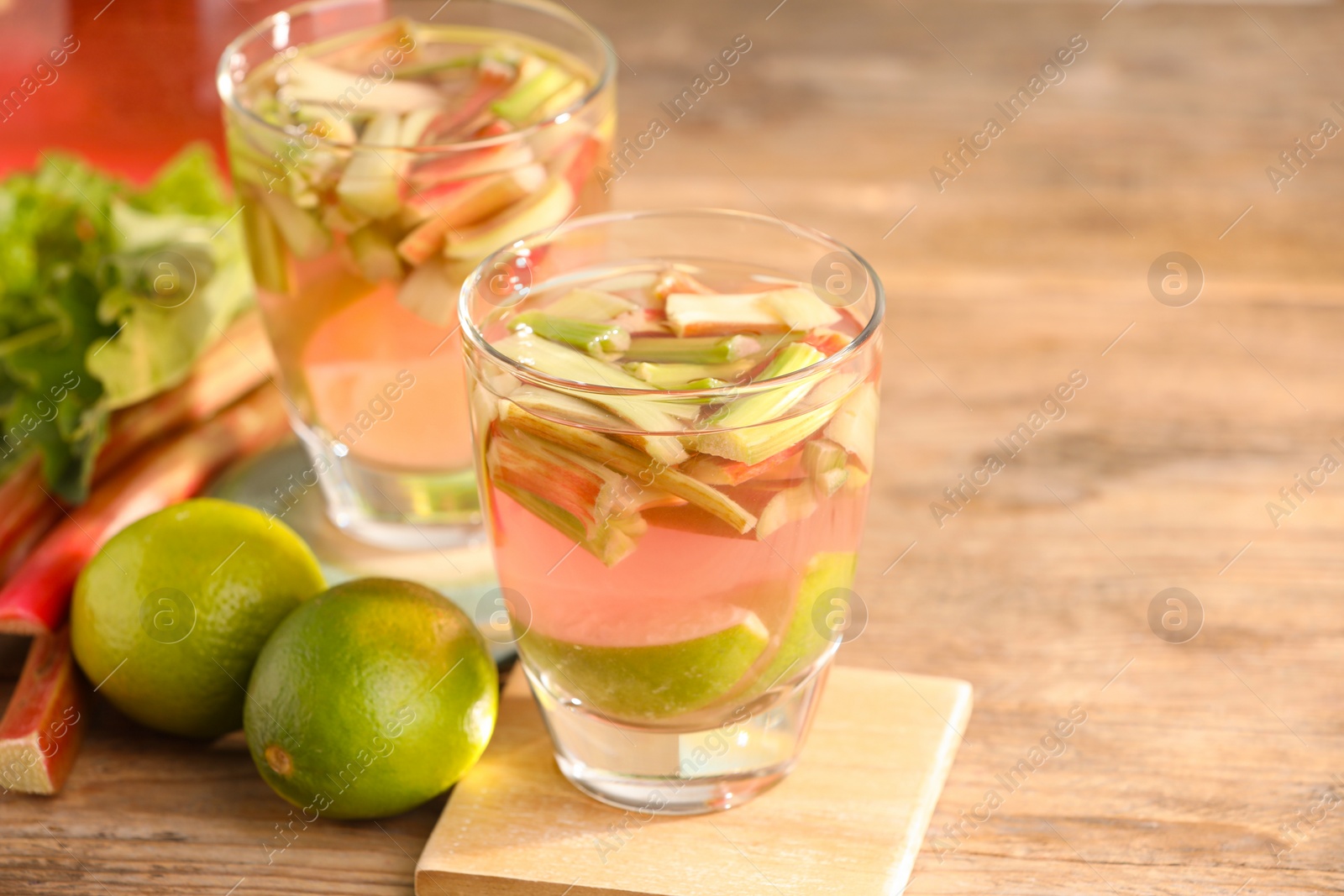 Photo of Glasses of tasty rhubarb cocktail and lime fruits on wooden table, closeup. Space for text