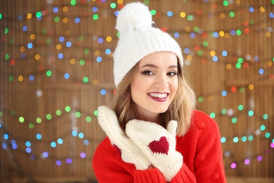Photo of Beautiful young woman in warm clothes posing on blurred lights background. Christmas celebration