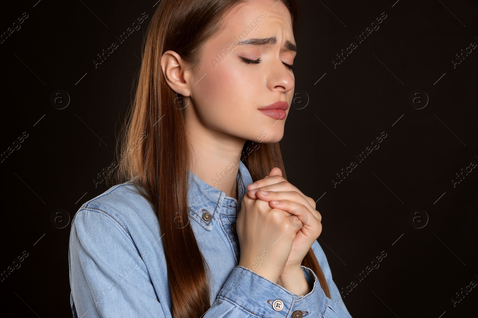 Photo of Woman with clasped hands praying on black background