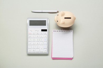 Calculator, piggy bank, notebook and pen on light grey background, flat lay