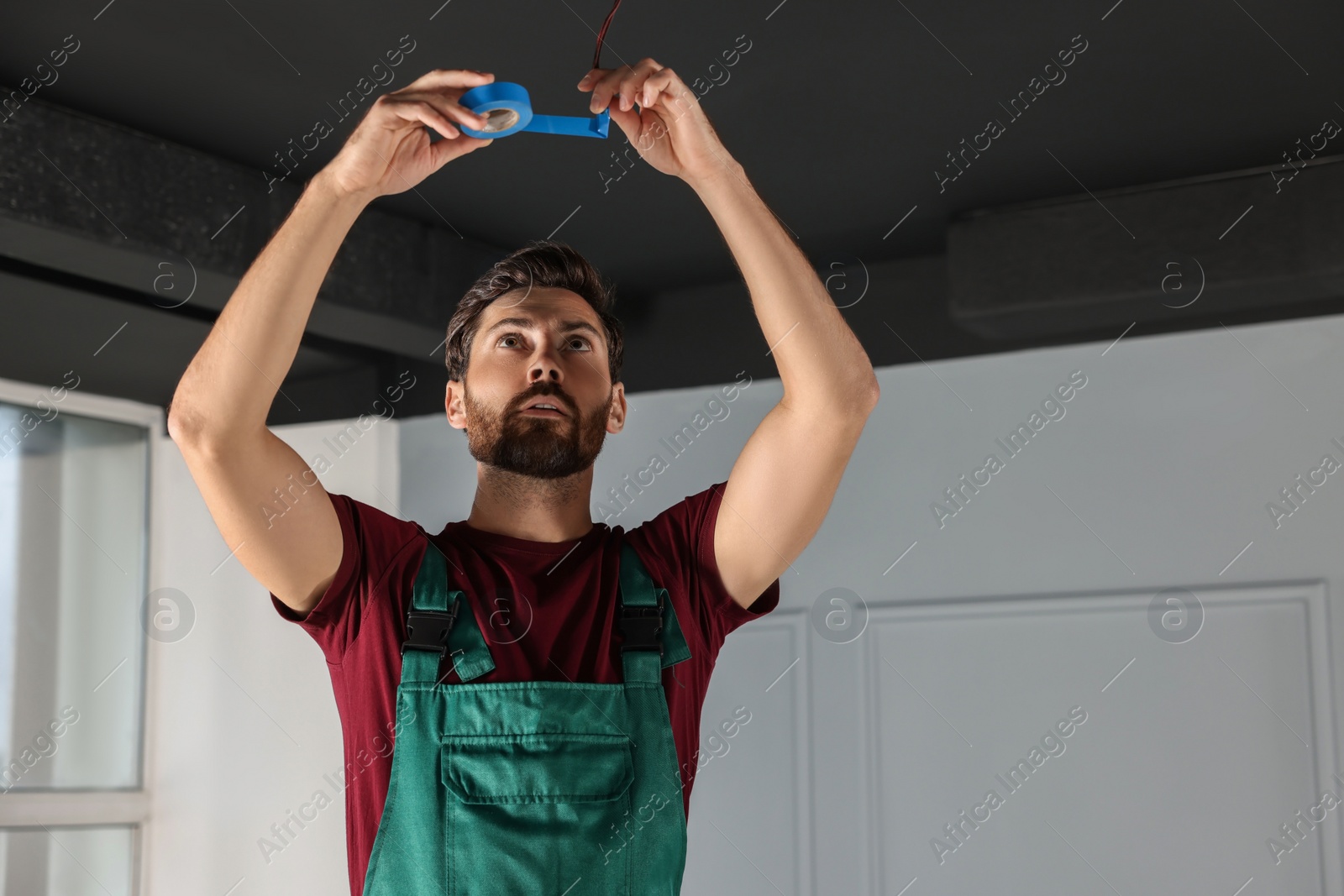 Photo of Electrician repairing ceiling wiring with insulting tape indoors