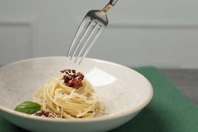Eating tasty spaghetti with sun-dried tomatoes and cheese from plate at table, closeup. Exquisite presentation of pasta dish